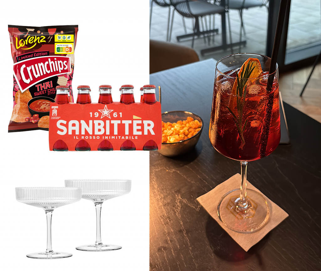 Ein Sanbitter Spritz in einem Weinglas auf dem Tisch mit einer Schüssel Erdnüsse. Daneben sind Produkte platziert